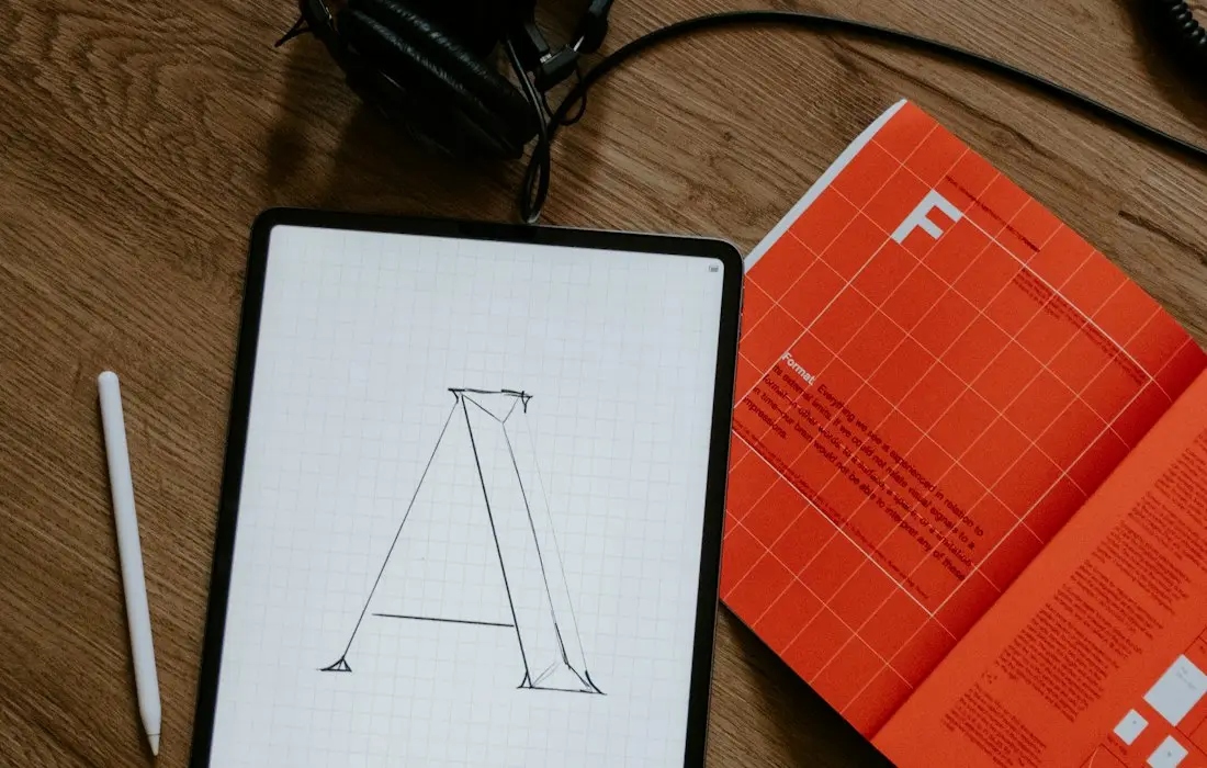 Typography sketch on a tablet beside a printed booklet